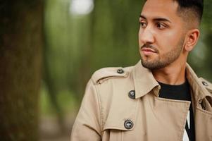 Stylish kuwaiti man at trench coat walking at park. photo