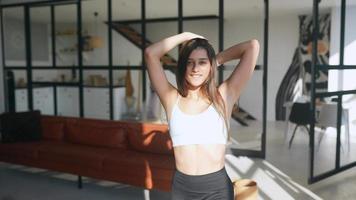 Fit young woman in leisure active wear puts hands in hair and dances in sunlight from window then flips hair video