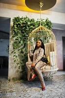 Young stylish african american woman in gold bird cage pose indoor. photo