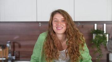 Young woman with long red curly hair looks at camera talking and laughing