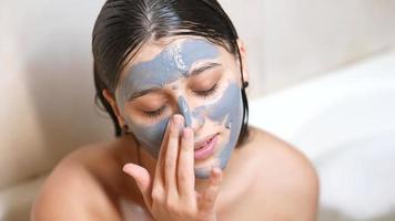 Young woman with wet hair applies clay mask to face video