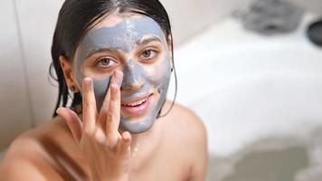mujer joven con el pelo mojado aplica máscara de arcilla a la cara