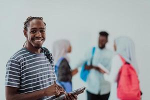 University lifestyle handsome young student man holding a tablet computer and smiling while standing against university with his friends have a team meeting in the background. High-quality photo