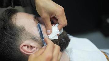 el peluquero usa una navaja de afeitar para afeitar el cuello y la cara del hombre para dar forma al vello facial video