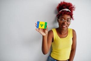 African american woman with afro hair, wear yellow singlet and eyeglasses, hold Saint Vincent and the Grenadines flag isolated on white background. photo