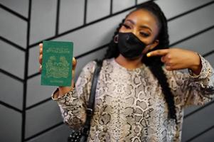 African woman wearing black face mask show Sierra Leone passport in hand. Coronavirus in Africa country, border closure and quarantine, virus outbreak concept. photo