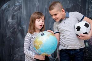 niño y niña usando el globo terráqueo frente a la pizarra foto