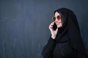 young muslim woman wearing sunglasses using smartphone photo