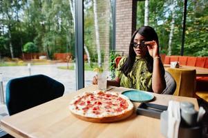 Glamour african american woman eating pizza at restaurant. photo