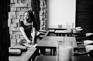 Lovely african american woman with dreadlocks in blue stylish jeans at cafe. Beautiful cool fashionable black young girl indoor. photo