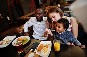 Happy multiethnic family with boy kid spend time at restaurant. Relationships of african man and white european woman. photo