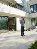 man using mobile phone in front of his luxury home villa photo