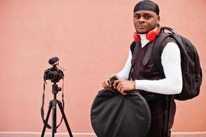 Young professional african american videographer holding professional camera with pro equipment. Afro cameraman wearing black duraq making a videos. photo