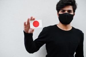 Asian man wear all black with face mask hold Japan flag in hand isolated on white background. Coronavirus country concept. photo