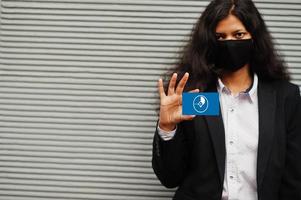 Asian woman at formal wear and black protect face mask hold Yap flag at hand against gray background. Coronavirus at country concept. photo