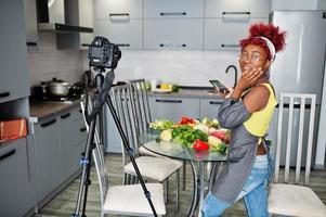 African american woman filming her blog broadcast about healthy food at home kitchen and making picture on phone. photo