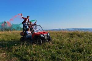 gente emocionada divirtiéndose disfrutando de un hermoso día soleado sosteniendo antorchas coloridas mientras conduce un coche de buggy fuera de la carretera foto