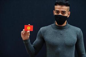 Middle eastern man in gray turtleneck and black face protect mask show Kyrgyzstan flag isolated background. photo