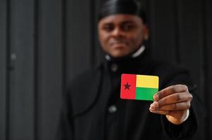 African man wear black durag hold Guinea-Bissau flag at hand isolated dark background. photo