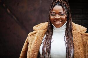 glamorosa mujer afroamericana en cálido abrigo de piel, anteojos posan en la calle. foto