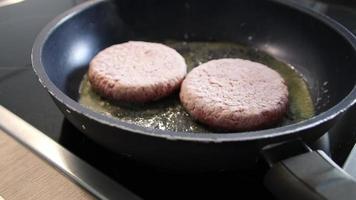 hamburguesas congeladas carne de hamburguesa chisporroteando en una sartén caliente con grasa y aceite como deliciosas albóndigas de barbacoa caseras como un almuerzo de comida rápida poco saludable con muchas calorías y colesterol en una sartén video