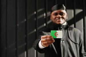 African man wear black durag hold Algeria flag at hand isolated dark background. photo