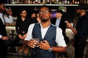 Stylish african american man against group of handsome retro well-dressed guys gangsters spend time at club, drinking on bar counter. Multiethnic male bachelor mafia party in restaurant. photo