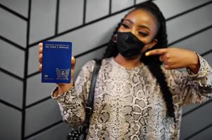 African woman wearing black face mask show Sao Tome and Principe passport in hand. Coronavirus in Africa country, border closure and quarantine, virus outbreak concept. photo