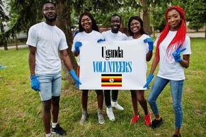 Group of happy african volunteers hold blank with Uganda flag in park. Africa countries volunteering, charity, people and ecology concept. photo