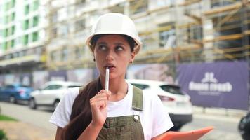 mujer con sombrero duro blanco en zona de construcción piensa y toma notas en papel video