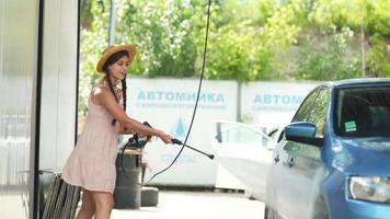 Young woman in pink dress and straw hat washes a car video