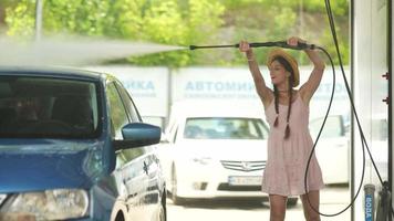 Young woman in pink dress and straw hat washes a car video