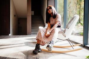 Fashion portrait of african american woman in long dress, boots and sunglasses indoor. photo