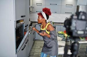 African american woman filming her blog broadcast about healthy food at home kitchen, bakes a cake in the oven. photo