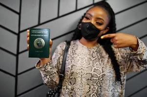 African woman wearing black face mask show Mali passport in hand. Coronavirus in Africa country, border closure and quarantine, virus outbreak concept. photo