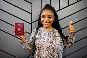 Close up portrait of young positive african american woman holding Peru passport and thumbs up. photo