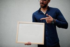 Middle eastern man wear blue shirt, eyeglasses, hold white empty board. photo