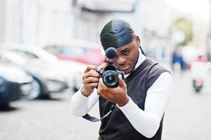 Young professional african american videographer holding professional camera with pro equipment. Afro cameraman wearing black duraq making a videos. photo