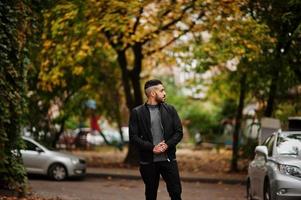 Portrait of stylish arab beard man wear grey turtleneck and black jaket. Arabian model guy on a background of autumn leaves. photo