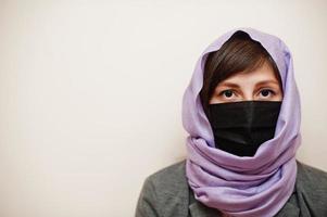 Portrait of young muslim woman wearing formal wear, protect face mask and hijab head scarf against isolated background. Coronavirus country concept. photo