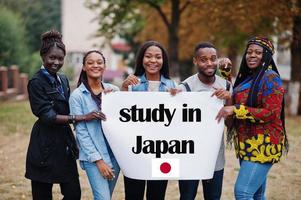 Study in Japan. Group of five african college students on campus at university yard hold white blank. Abroad countries for student concept. photo