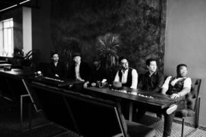 Group of handsome retro well-dressed man gangsters spend time at club. Multiethnic male bachelor mafia party in restaurant, sitting by table. photo