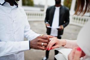 Wedding engagement ceremony with pastor. Multiethnic couple put ring each other. Relationships of african man and white european woman. photo