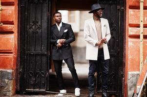 dos hombres negros de moda. retrato de moda de modelos masculinos afroamericanos. llevar traje, abrigo y sombrero.