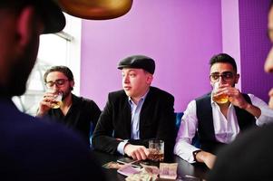 Group of handsome retro well-dressed man gangsters spend time at club, sitting and drinking whiskey. Multiethnic male bachelor mafia party in restaurant. photo