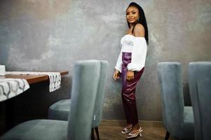 Beautiful african american woman in white blouse and red leather pants pose at restaurant. photo