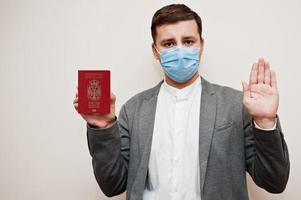 European man in formal wear and face mask, show Serbia passport with stop sign hand. Coronavirus lockdown in Europe country concept. photo