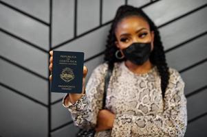 mujer afroamericana con mascarilla negra muestra el pasaporte de costa rica en la mano. coronavirus en el país de América, cierre de fronteras y cuarentena, concepto de brote de virus. foto