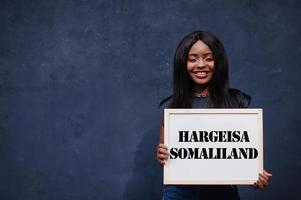 mujer africana sostiene una pizarra blanca con la inscripción hargeisa somalilandia. concepto de ciudad más poblada de África. foto