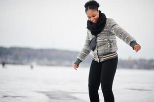 mujer africana vestida con bufanda negra posada en un lago de hielo congelado, día de invierno en europa. foto